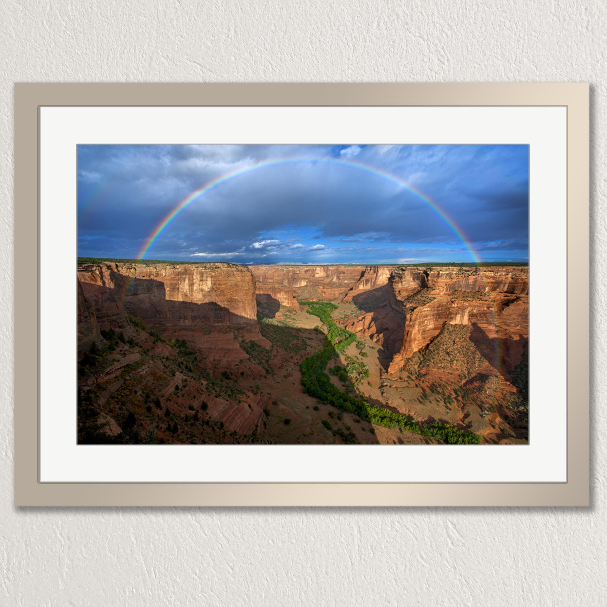 A framed photograph depicting a stunning canyon landscape with a vibrant rainbow arching across the sky above the rugged, rocky terrain.