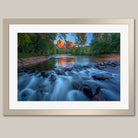 A framed photograph depicting a serene river flowing through a lush, forested landscape, with a large rock formation visible in the distance.
