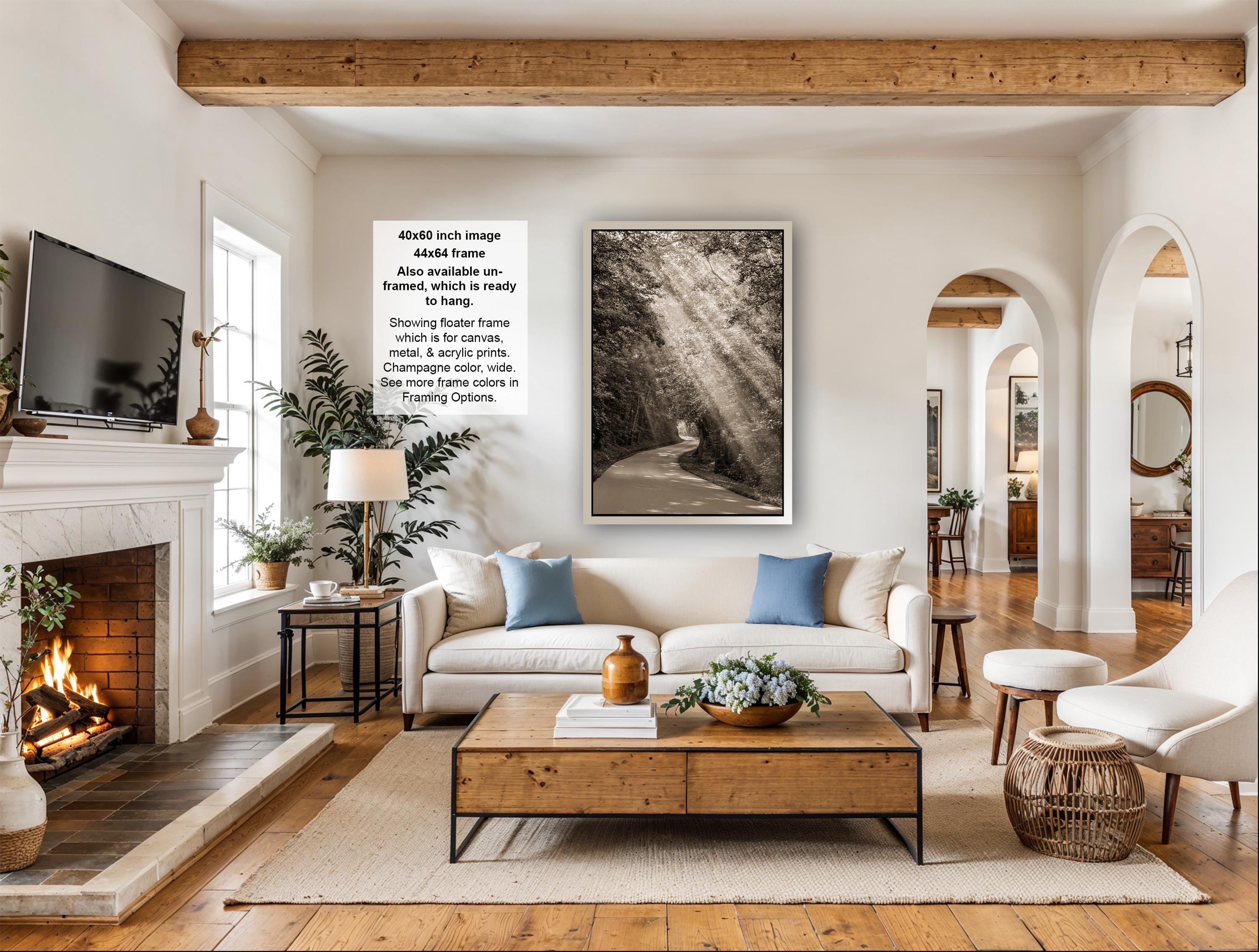 a cozy living room with a fireplace, a large window, a white sofa, a wooden coffee table, and a framed photograph of a forest.