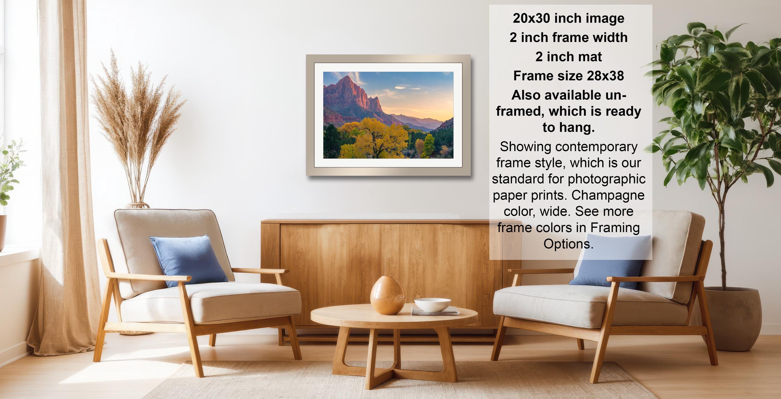 a living room with a wooden coffee table, two white armchairs, and a framed landscape painting hanging on the wall.