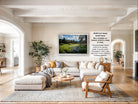 The image is a large framed picture of a field with trees and flowers hanging on the wall of a living room.