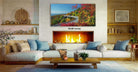 a cozy living room with a fireplace, a large framed landscape painting depicting a winding road through a forest, and a wooden coffee table in front of the fireplace.