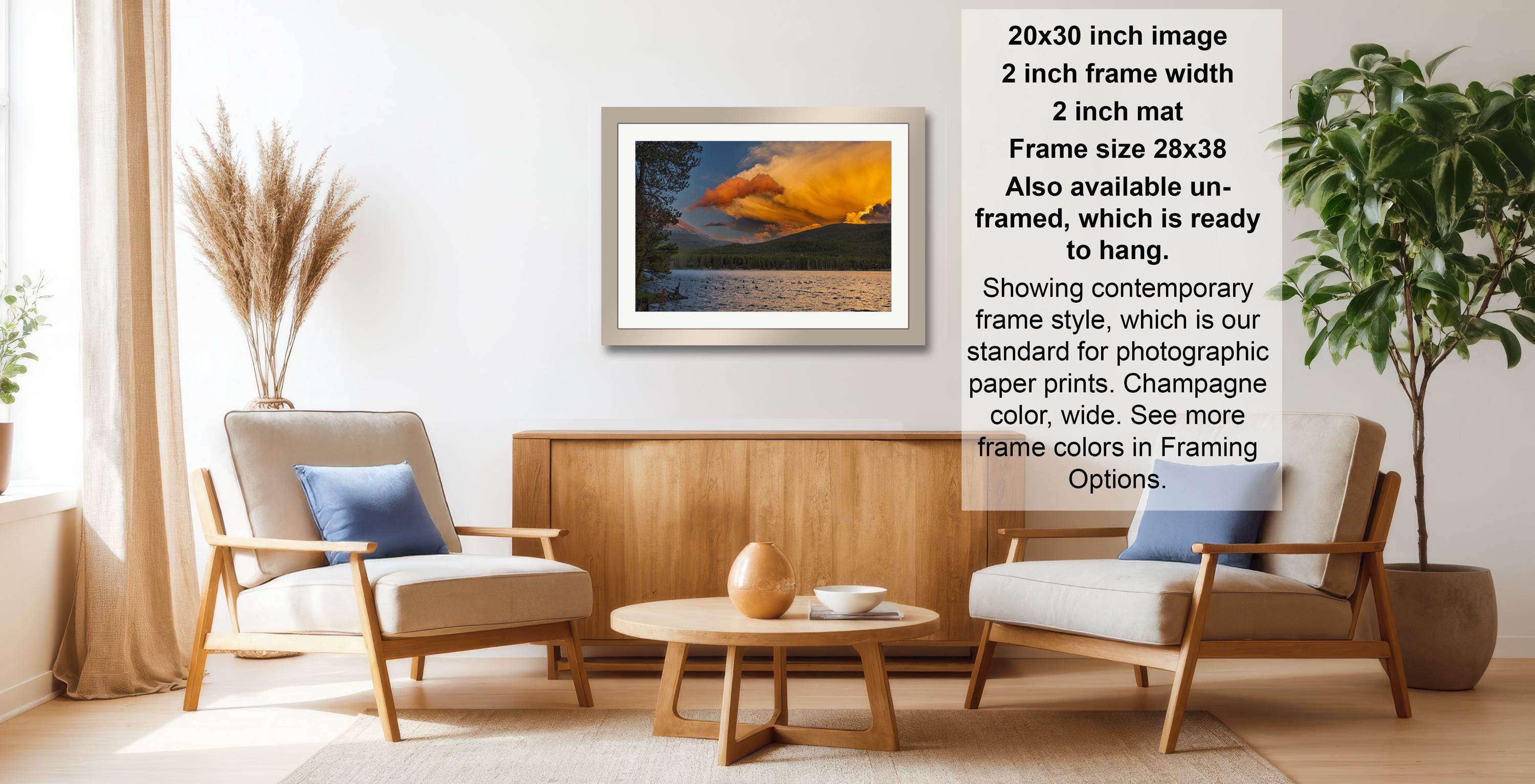 a living room with a framed landscape photograph hanging on the wall, a wooden coffee table in the center, and two chairs facing each other.