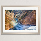 A framed photograph depicting a stunning natural landscape with a waterfall cascading down a steep, rocky cliff face, creating a vibrant rainbow in the mist.