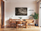 a cozy dining room with a wooden table and chairs, a large framed black and white photograph of a forest scene hanging on the wall, and a potted plant and vase on the table.