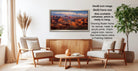 a living room with a large framed landscape painting hanging on the wall. The painting depicts a desert scene with mountains in the background. The room has two armchairs and a coffee table, creating a cozy and inviting atmosphere.