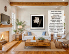 The image is a living room with a fireplace, a white sofa, a wooden coffee table, and a framed black and white photograph of a flower hanging on the wall.