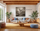 a cozy living room with a large, black and white photograph of a tree hanging on the wall. The room is furnished with a gray sofa, a wooden coffee table, and several potted plants. The photograph is approximately 54.54 inches in size.