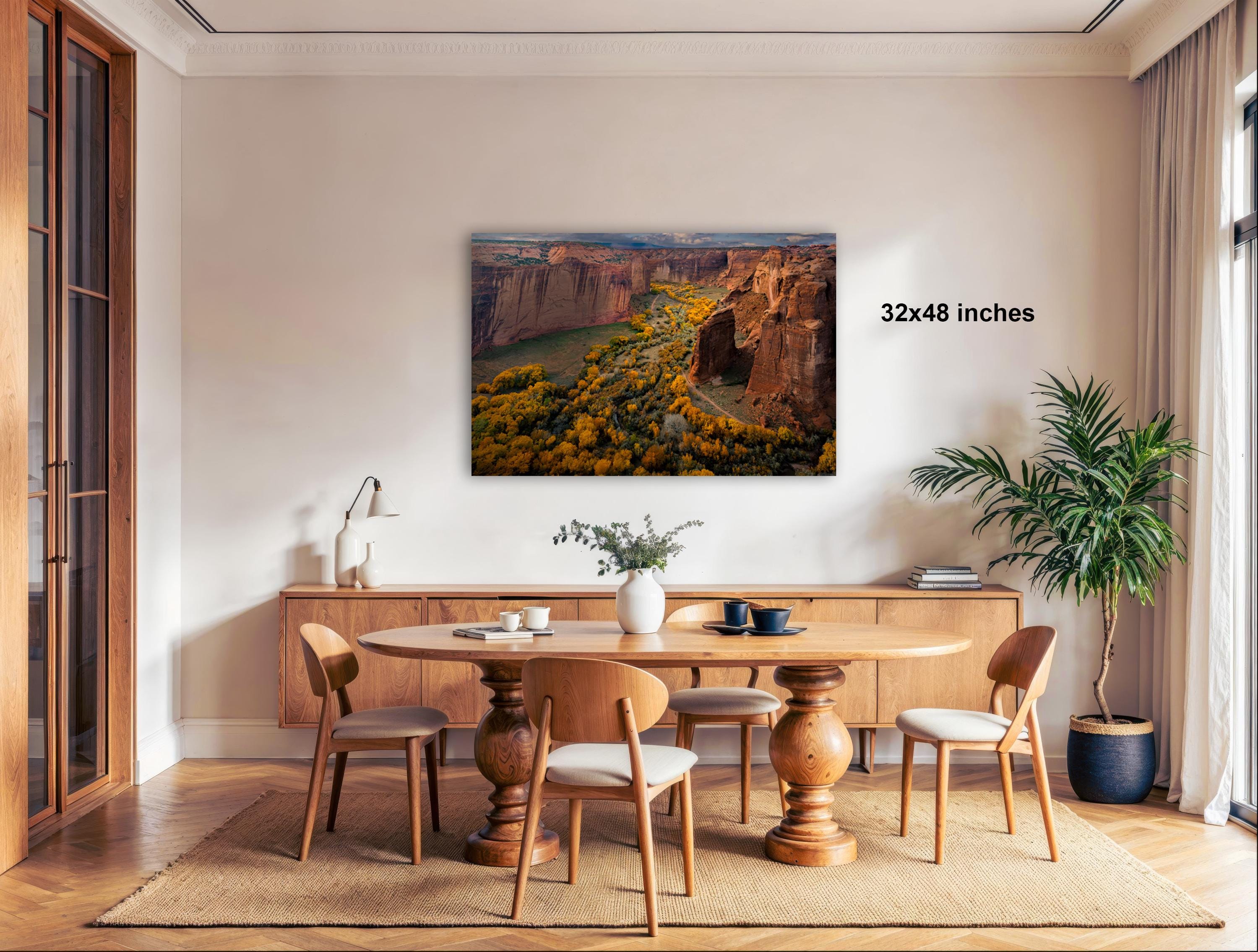 a large, framed landscape painting hanging on a wall above a wooden dining table with chairs.