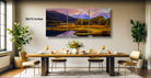 a large, three-panel landscape painting hanging on a wall above a wooden dining table set with wine glasses, plates, and a vase of flowers.
