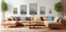 The image is a modern living room with a large sectional sofa, a coffee table, and several potted plants. The walls are decorated with framed artwork depicting a forest scene, and the furniture is arranged to create a comfortable and inviting atmosphere.