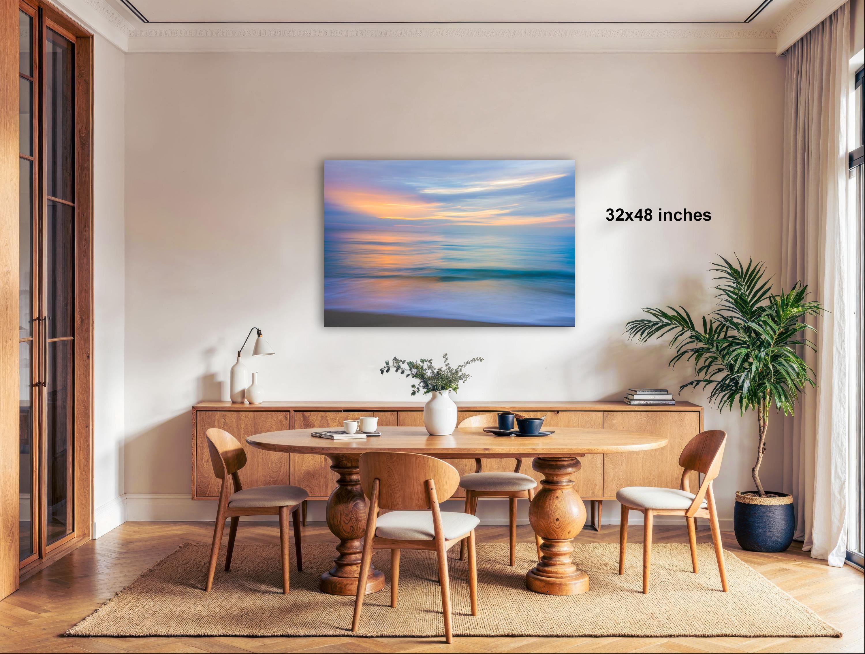 a serene dining room with a large wooden table surrounded by matching chairs. A painting of a sunset is displayed on the wall above the table, creating a warm and inviting atmosphere. The room is decorated with various items, including a potted plant, a vase, and a lamp, adding to the overall ambiance.