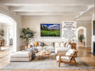 The image is a large framed picture of a scenic landscape hanging on a wall in a spacious living room.