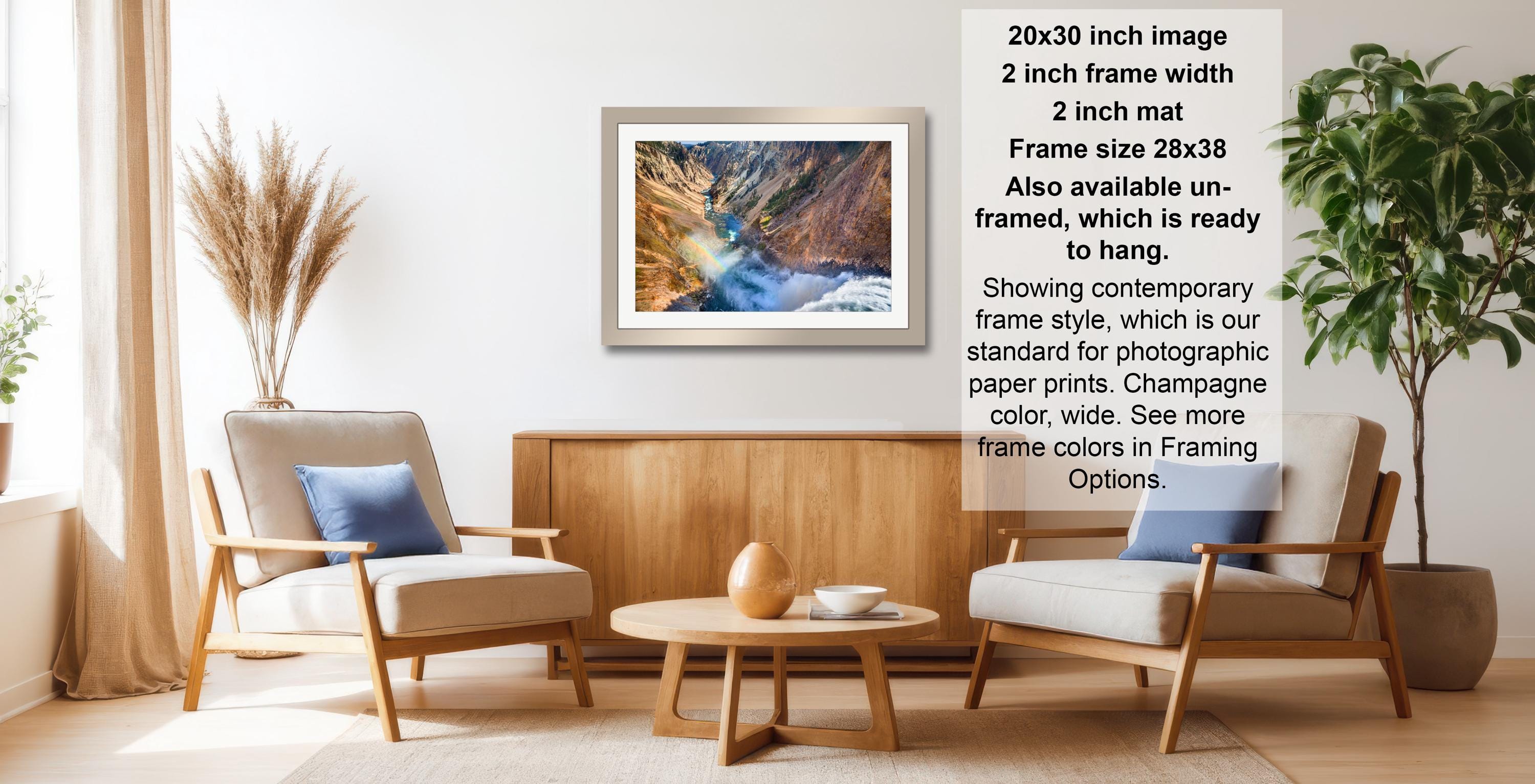 a living room with a wooden coffee table, two white armchairs, and a framed landscape photograph hanging on the wall.