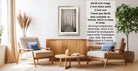a living room with a framed photograph of a forest scene hanging on the wall. The room has two armchairs, a coffee table, and a potted plant, creating a cozy and inviting atmosphere.