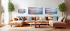 A modern living room with a large sectional sofa, a coffee table, and three framed landscape paintings on the wall.