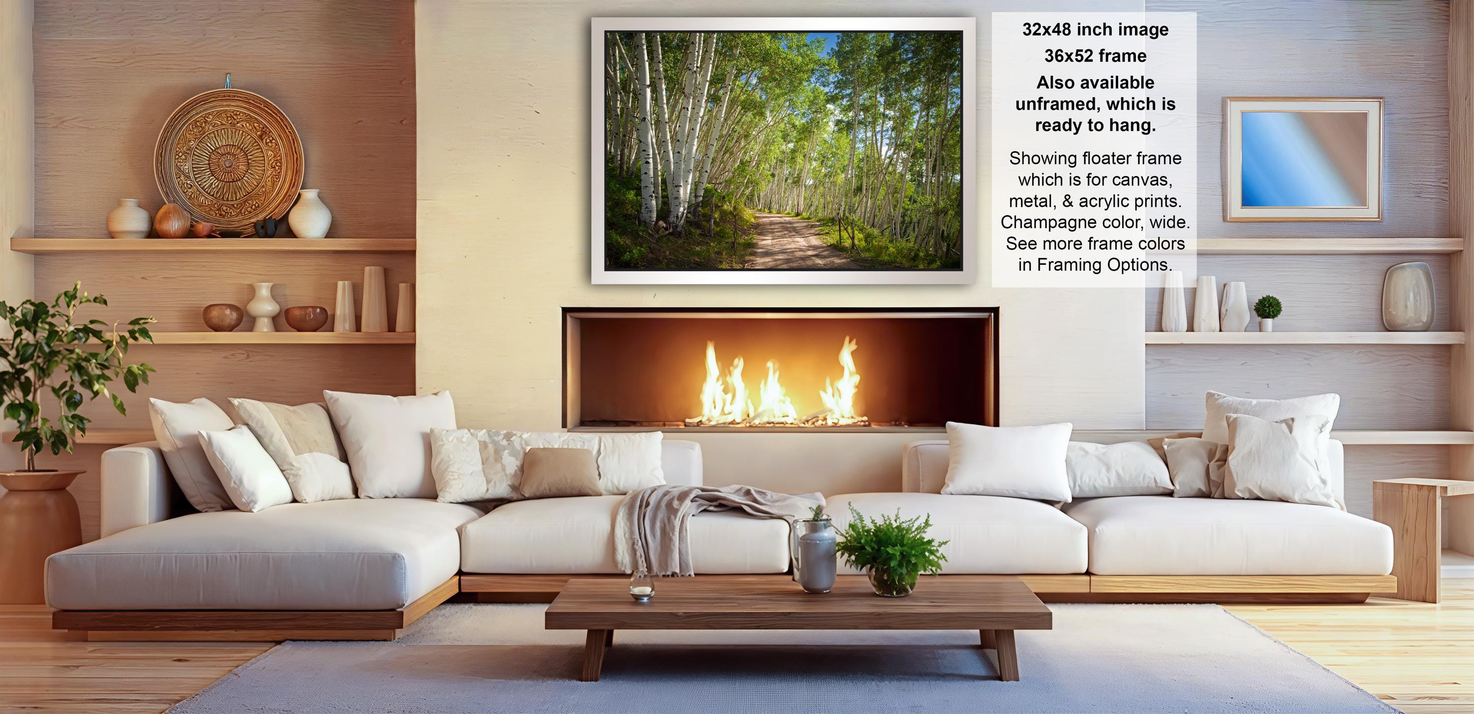 a cozy living room with a fireplace, white sofas, and a coffee table. The room has a warm and inviting atmosphere, with a fireplace providing a focal point and a painting of a forest path above it. The furniture and decor create a harmonious and comfortable space for relaxation and socializing.