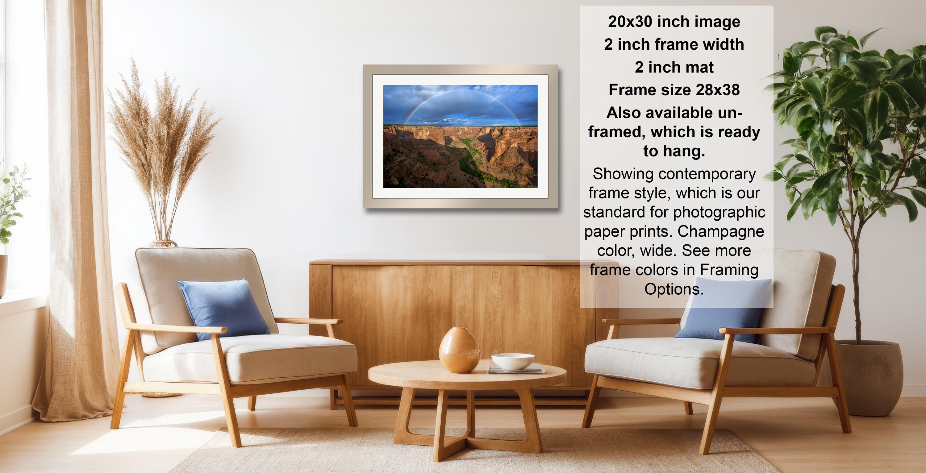 a living room with a framed landscape photograph hanging on the wall, a wooden coffee table in the center, and two chairs facing each other.