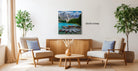 a living room with a large painting of a mountain lake and boats hanging on the wall. The painting is 30 inches wide. The room is furnished with two chairs and a coffee table, creating a cozy and inviting atmosphere.