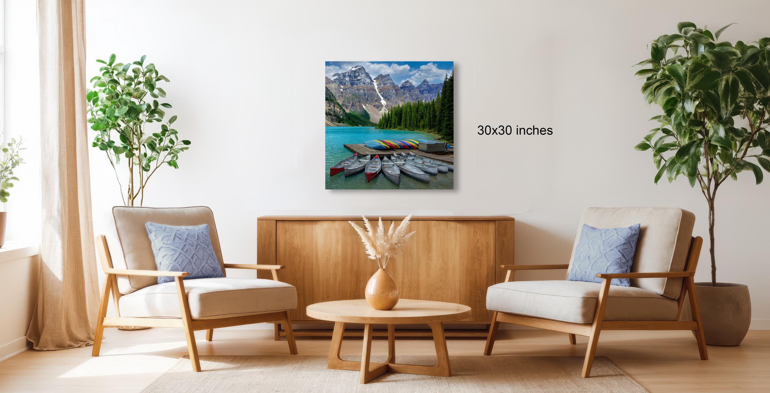 a living room with a large painting of a mountain lake and boats hanging on the wall. The painting is 30 inches wide. The room is furnished with two chairs and a coffee table, creating a cozy and inviting atmosphere.