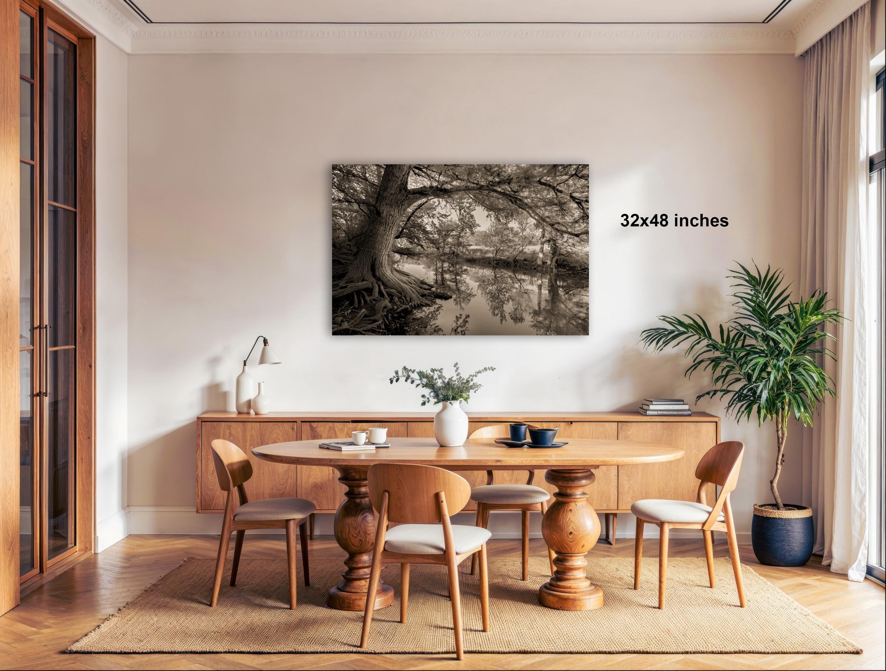 a cozy dining room with a wooden table and chairs, a potted plant, and a large framed black and white photograph of a tree on the wall.