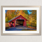 A red wooden covered bridge with a diamond pattern on the roof, surrounded by colorful autumn foliage, is the focal point of the image.