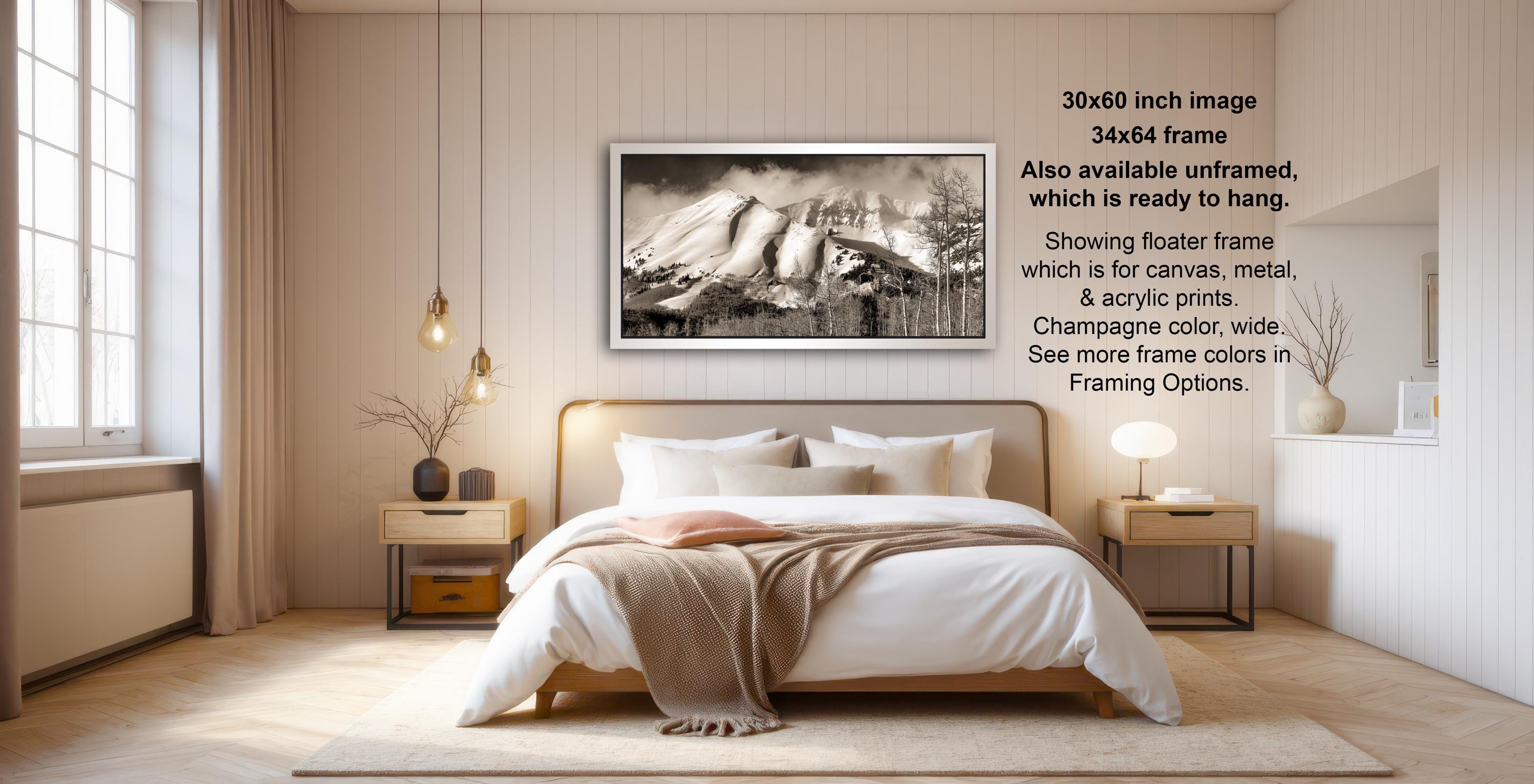 A modern bedroom with a large bed, nightstands, and a framed black and white photograph of a snowy mountain landscape hanging on the wall.