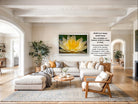 The image is a large, high-quality photograph of a living room with a large, framed picture of a yellow flower on the wall. The room has a neutral color scheme with white walls, a wooden floor, and a comfortable seating area with a sofa and armchairs. There are also several potted plants and decorative items, such as a vase and a bowl, adding to the cozy and inviting atmosphere of the space.