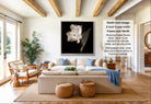 A modern living room with a large white sofa, a wooden coffee table, and a potted plant. The room has a minimalist and clean design, with a large framed black and white photograph of a flower hanging on the wall.