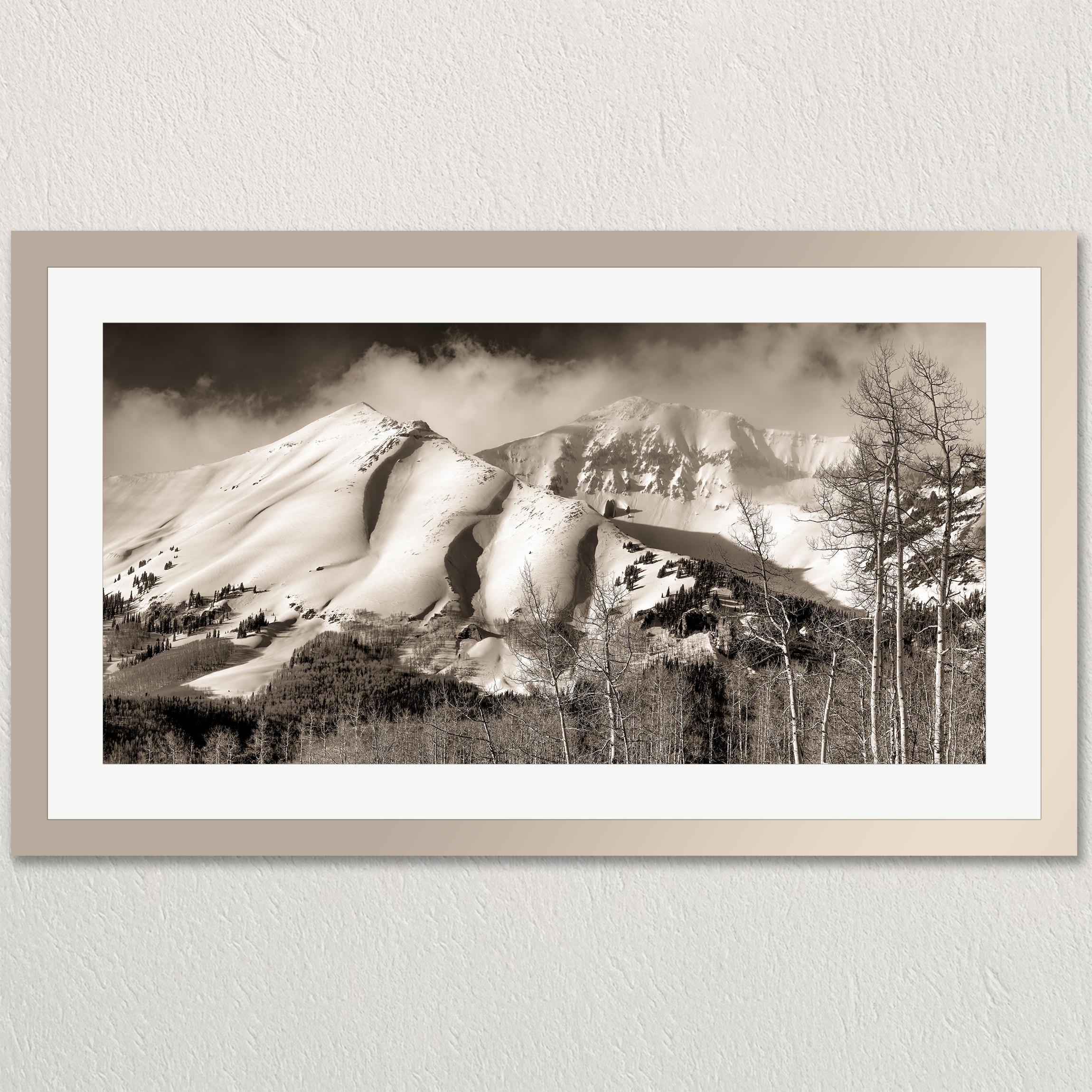 A black and white photograph of a snow-covered mountain range with a cloudy sky in the background.