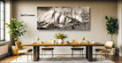 a large black and white photograph of a mountain landscape, which is hanging on the wall above a wooden dining table set with wine glasses, plates, and a vase of flowers.