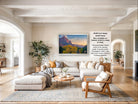 The image is a large framed picture of a mountainous landscape, hanging on a wall in a spacious living room.