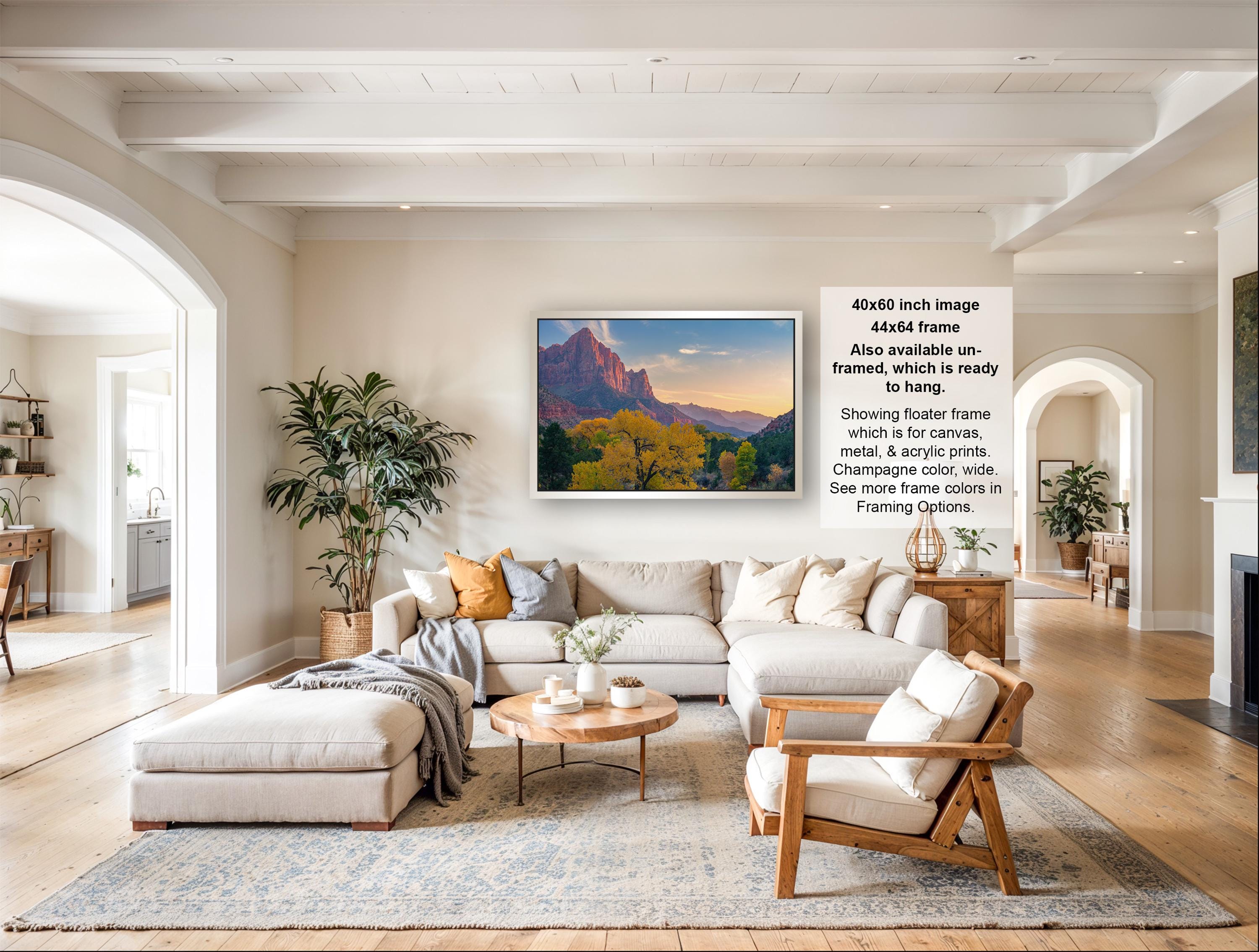 The image is a large framed picture of a mountainous landscape, hanging on a wall in a spacious living room.