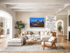 a large, modern living room with a comfortable sectional sofa, a coffee table, and a fireplace. The room has a neutral color scheme with white walls and a gray rug. A large framed landscape painting depicting a mountain range is hanging on the wall, adding a touch of nature and color to the space.